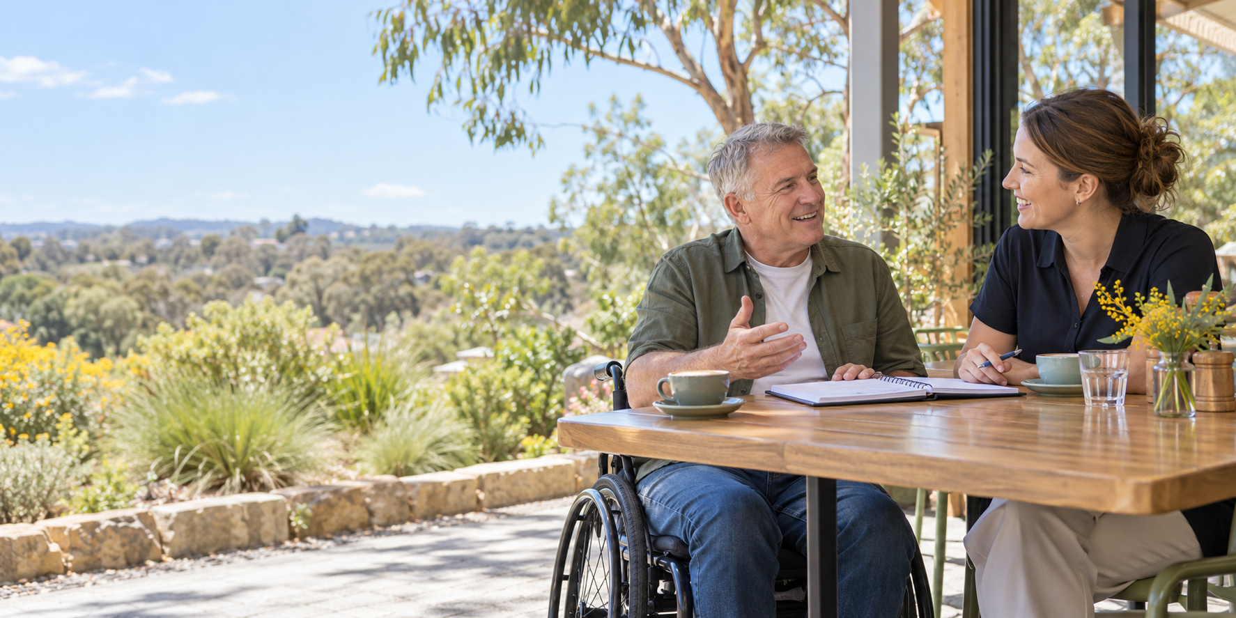 A man using a wheelchair talking about goals with a support worker at a cafe